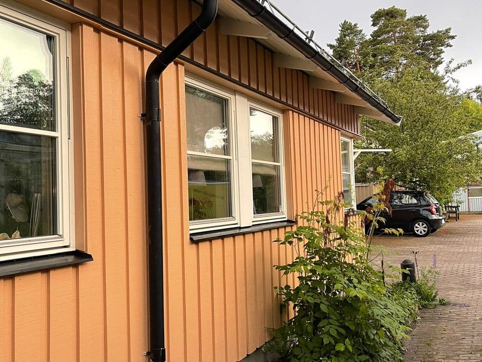 Långsida på ett hus med laxrosa stående panel, vita fönster och svart stuprör